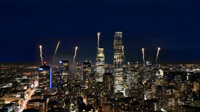 A city skyline at night with fireworks rising between the towers